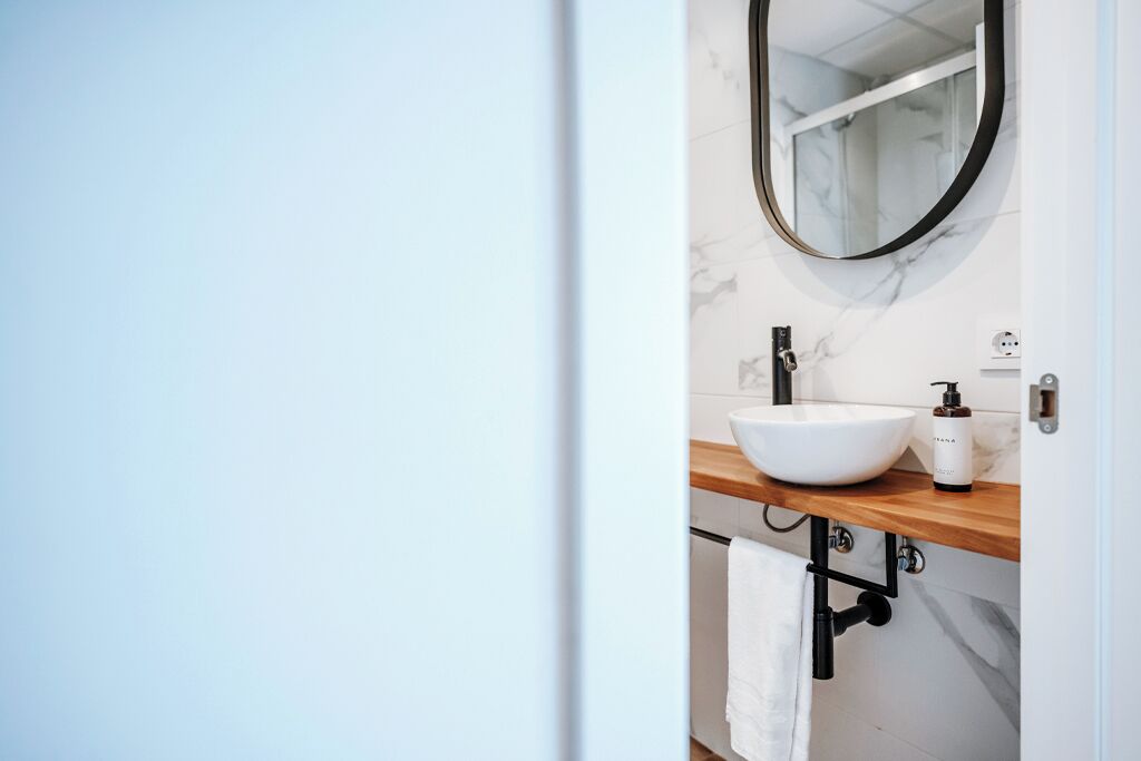 A bathroom with a white sink, a wooden countertop, a black faucet, a mirror, and a towel hanging on a rack.