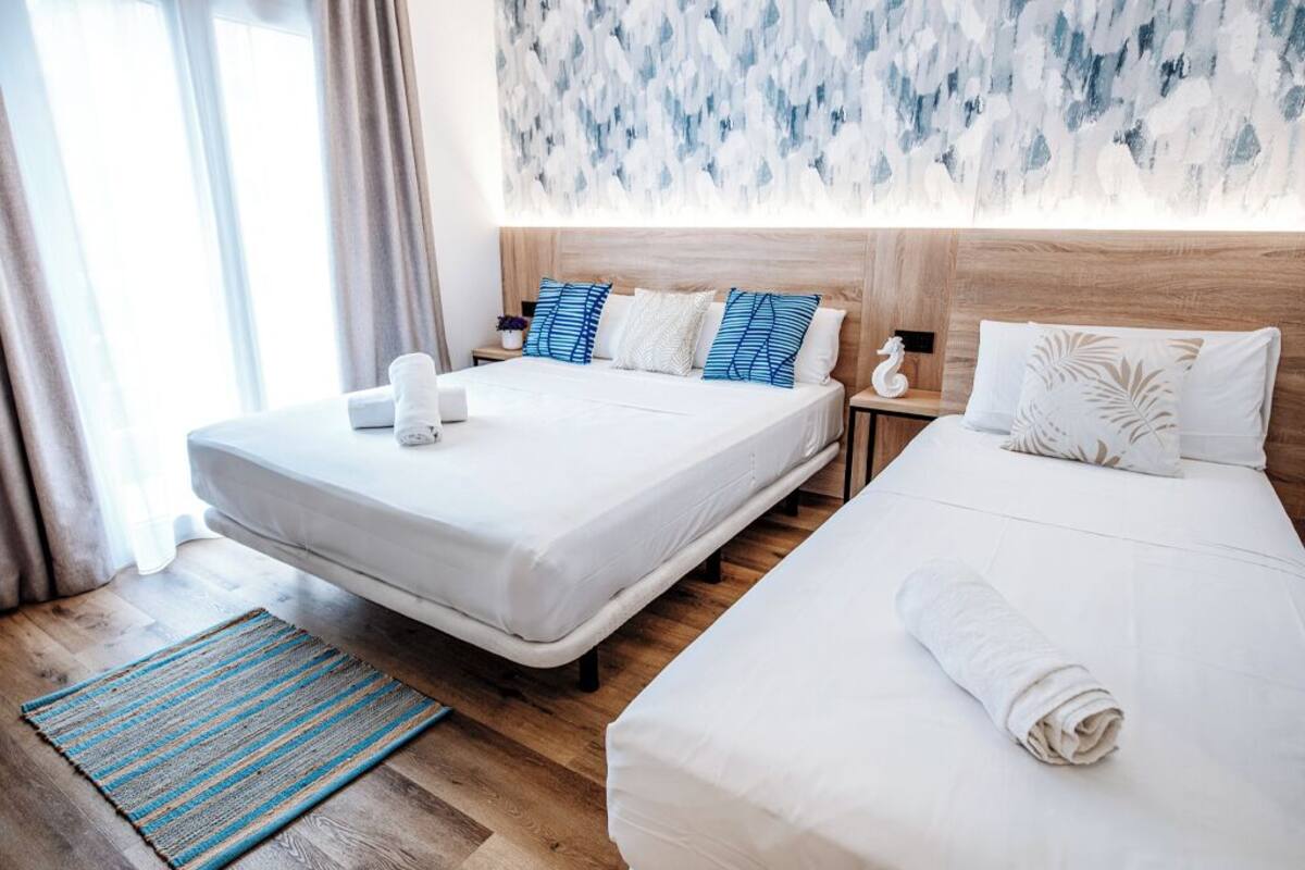 A hotel room with two beds, a wooden headboard, a blue abstract wall art, and a striped rug.