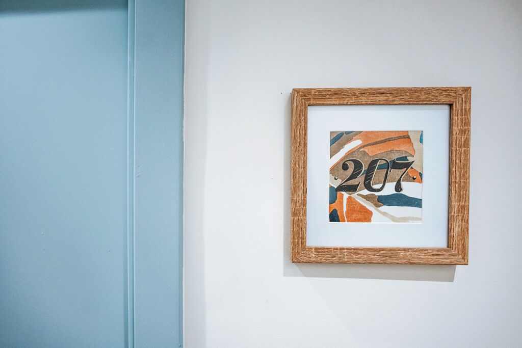 A framed abstract artwork with the number '207' on a white wall.