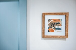 Obra de arte abstracta enmarcada con el número '207' sobre una pared blanca.