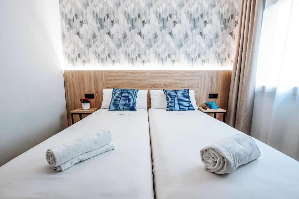 A double bed with white linens, two blue and white pillows, and two rolled towels.