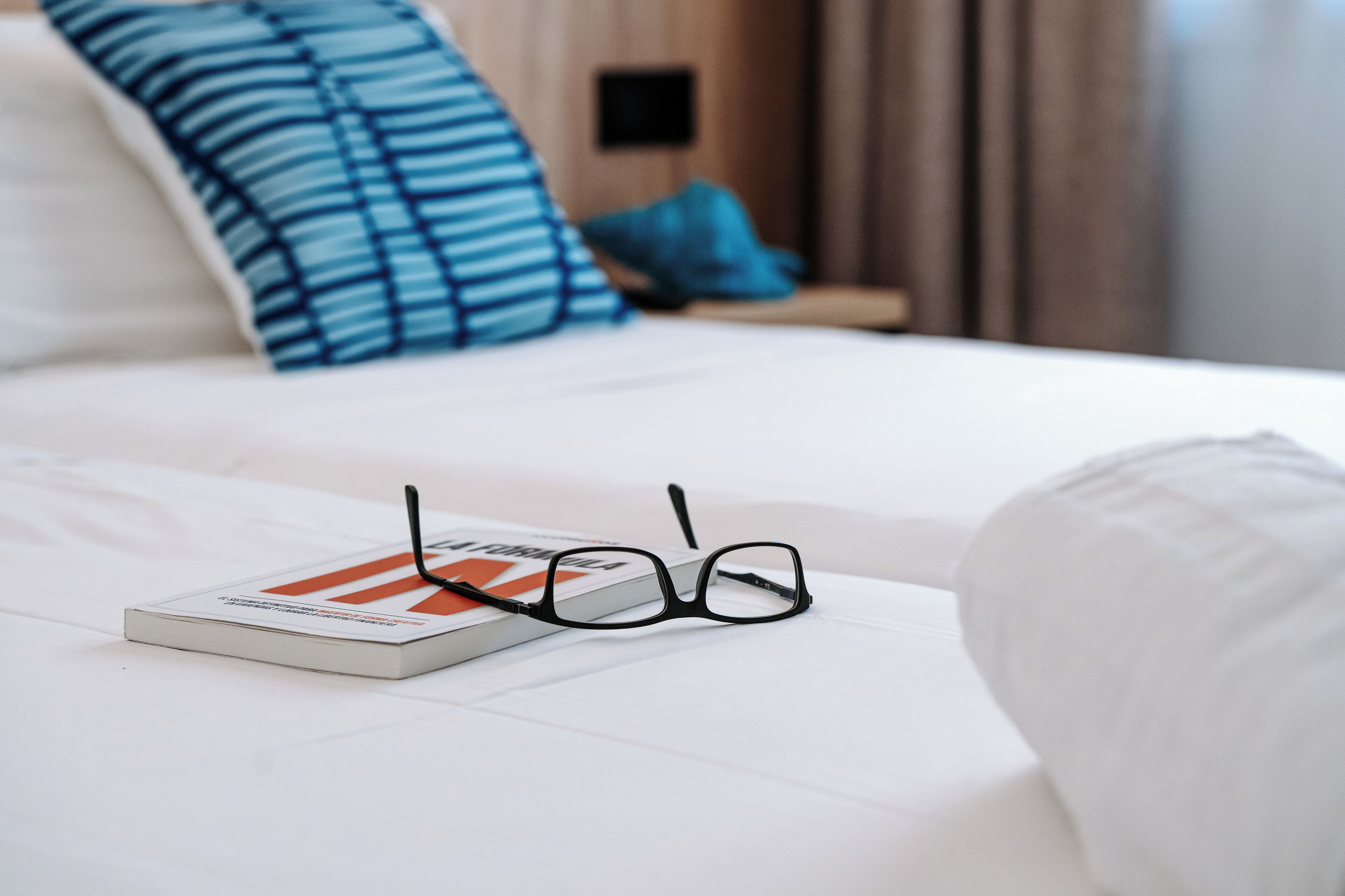 Un lit bien fait, avec un livre et des lunettes posés dessus.