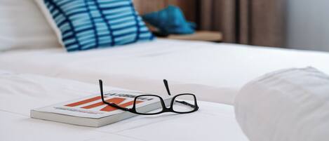 A neatly made bed with a book and glasses on it.