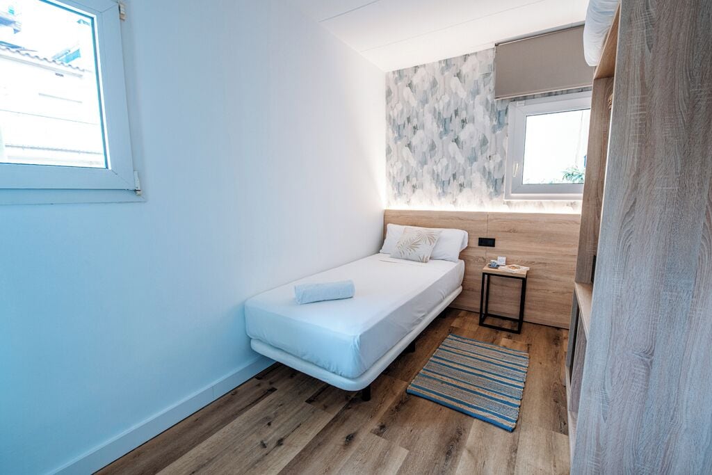 A modern bedroom with a single bed, a small bedside table, a window, and a patterned wall.