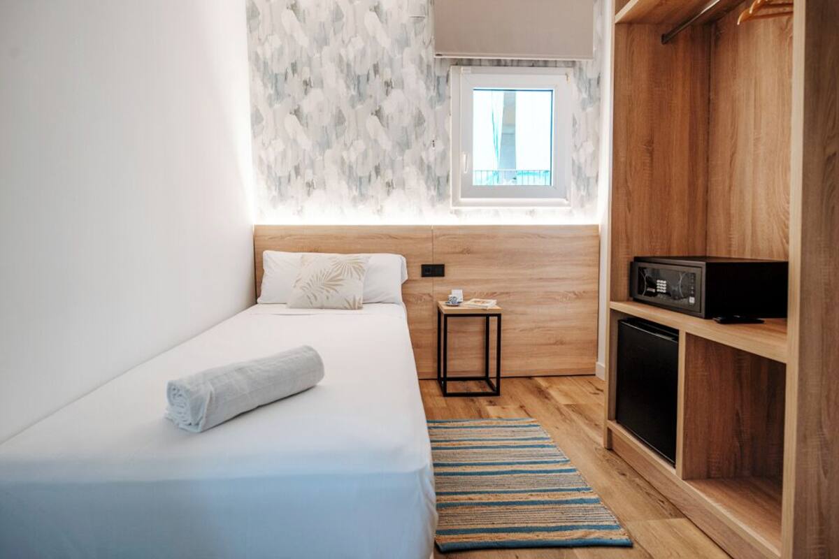 A compact hotel room with a single bed, a small bedside table, a microwave, and a wooden cabinet.