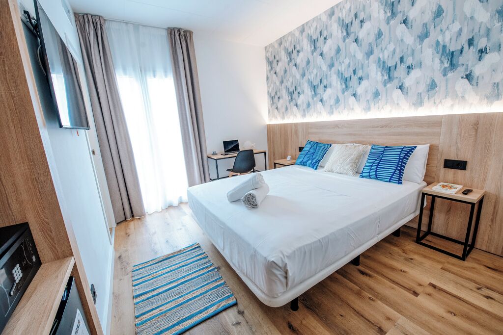 Une chambre d’hôtel avec un grand lit, un bureau avec un ordinateur, un téléviseur fixé au mur et une fenêtre avec des rideaux.