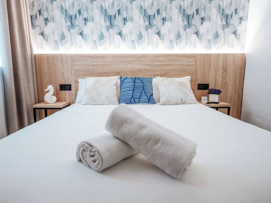 Una cama bien hecha con cabecera de madera, almohadas estampadas en blanco y azul, y una toalla enrollada sobre la cama.