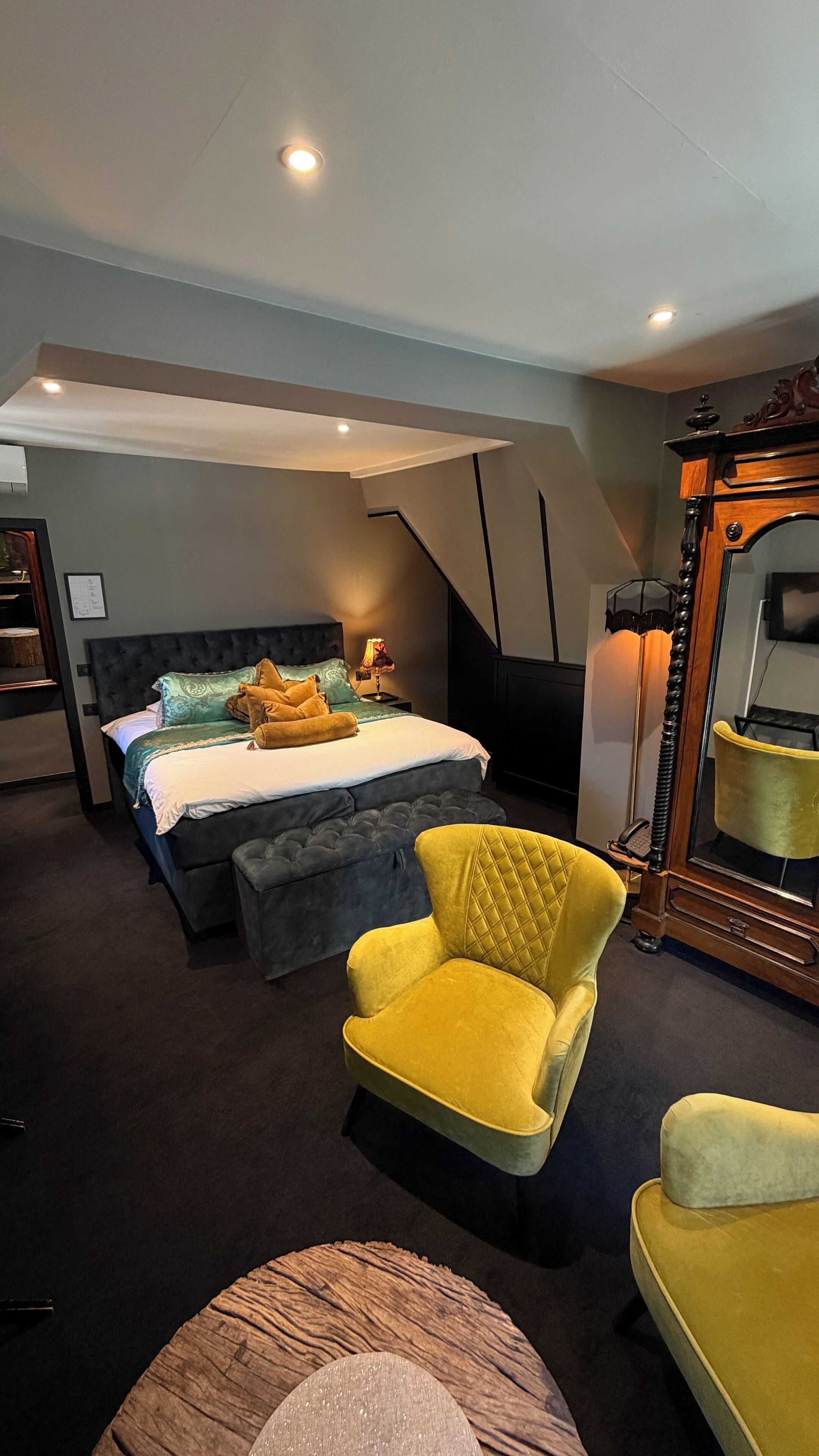 A bedroom with a bed, a yellow armchair, a wooden dresser, and a mirror.