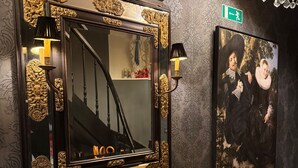 Un canapé noir agrémenté de coussins décoratifs, un grand miroir orné de motifs dorés et un portrait encadré accroché au mur.