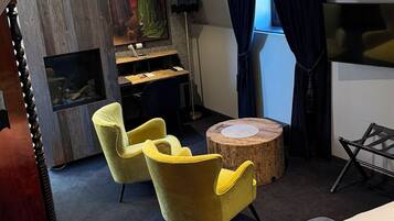 A hotel room with a bed, two yellow armchairs, a round wooden table, a desk with a computer, and a painting on the wall.