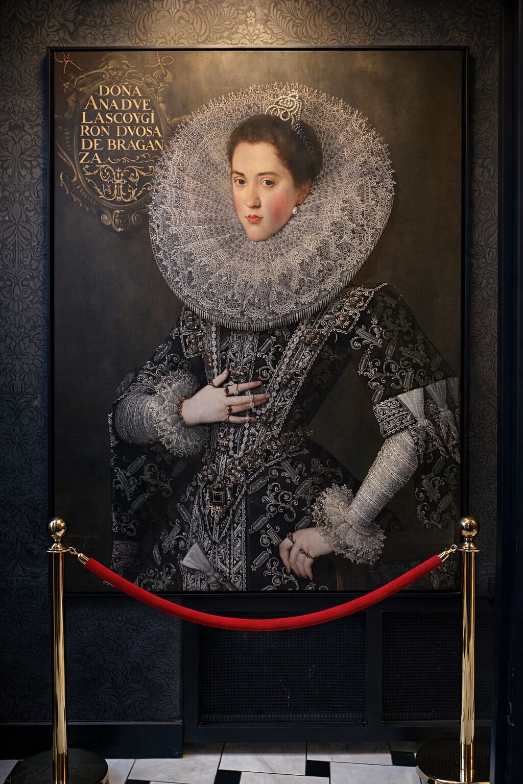 Retrato emoldurado de uma pessoa vestida com trajes históricos, com uma barreira de corda vermelha na frente.