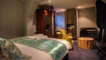 A bedroom with a large bed, a wooden wardrobe, a yellow armchair, a round wooden stool, and a desk with a chair.