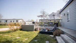 A backyard with a wooden deck, two outdoor umbrellas, a dog, and a small garden area. - Gemütliches Chalet im Ferienpark de Oase Renesse (Renesse)