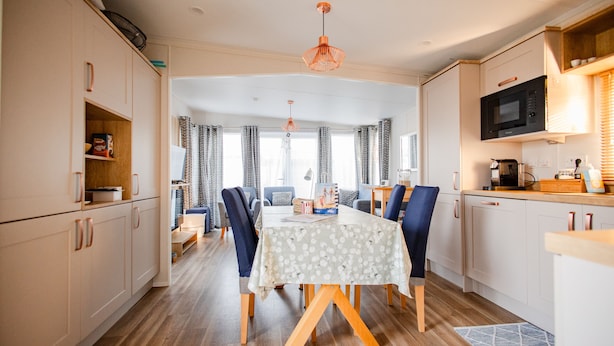 A modern kitchen with white cabinets, a dining table with blue chairs, and a microwave. - Gemütliches Chalet im Ferienpark de Oase Renesse (Renesse)