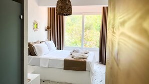 Une chambre à coucher avec un lit, une lampe de chevet, une fenêtre avec des rideaux et une vue sur la verdure à l’extérieur.
