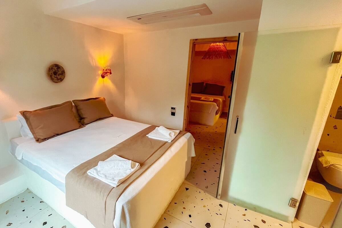 A hotel room with a bed, bedside lamps, a door leading to a bathroom, and a small table.