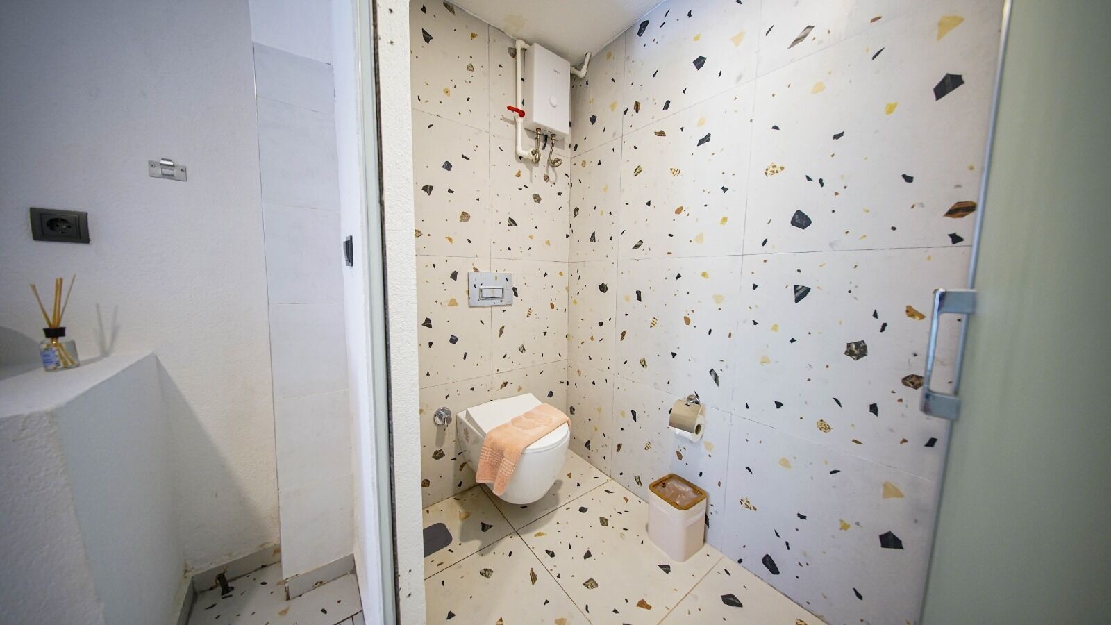 A bathroom with a white toilet, a shower, and a sink. The walls are covered with a terrazzo tile pattern.
