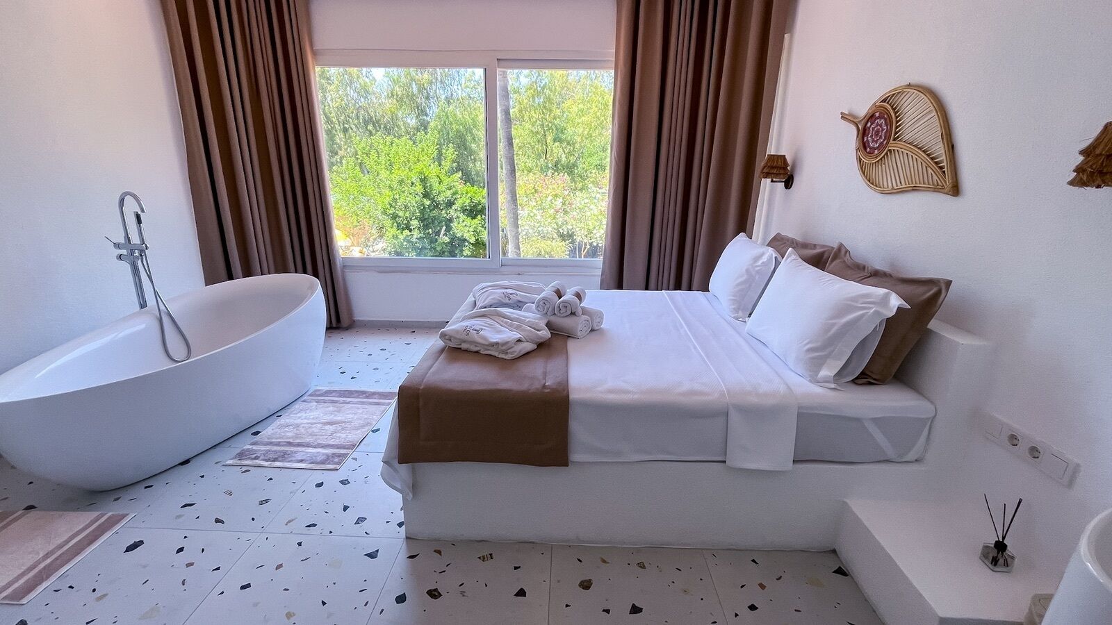 Un baño moderno con una bañera independiente, una cama grande con ropa de cama blanca y vistas a zonas verdes.