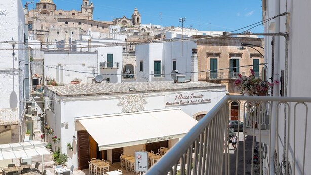 A rooftop terrace with outdoor seating, a restaurant named 'L'Antica Locanda' offering pizza, and a view of historic buildings in the background. - Casa Mila (Ostuni)