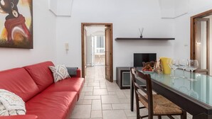 A modern living room with a red sofa, a glass dining table, and a TV. - Casa Mila (Ostuni)
