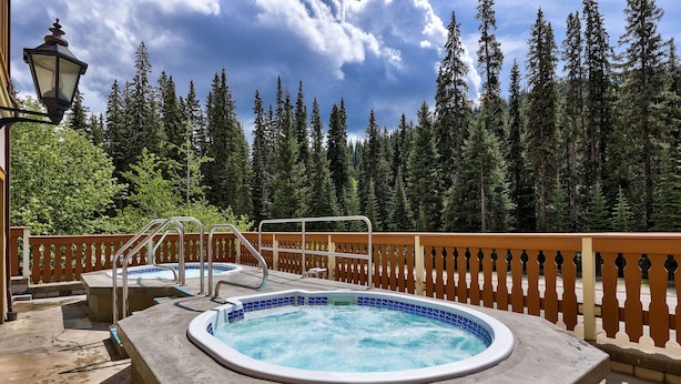 A hot tub with a wooden deck and a railing, surrounded by a forest. - Hearthstone Lodge #336 (Sun Peaks)