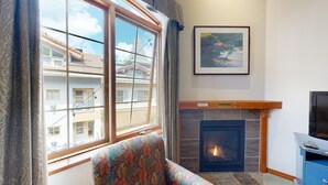 A room with a fireplace, a sofa, a television, and a window with curtains. - Hearthstone Lodge #336 (Sun Peaks)
