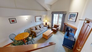 A living room with a sofa, a wooden coffee table, a patterned armchair, a small table with a lamp, and a fireplace. - Hearthstone Lodge #336 (Sun Peaks)