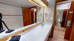 A bathroom with a large mirror, two sinks, a hairdryer, and a tripod in the corner. - Hearthstone Lodge #336 | 3 Peaks Rentals (Sun Peaks)