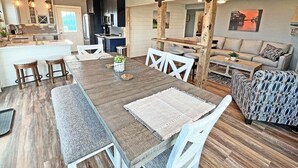 Zona d'estar àmplia amb una taula de dinar de fusta, cadires blanques i un sofà estampat.