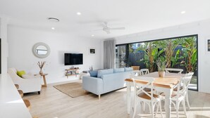 A modern living room with a sofa, TV, and dining area with a table and chairs. - Beach Pad on Nautilus (Kingscliff)
