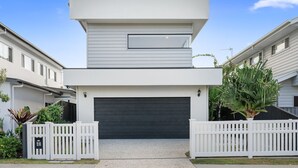 A modern two-story house with a dark garage door, white picket fences, and a small driveway. - Beach Pad on Nautilus (Kingscliff)