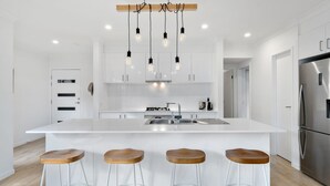 A modern kitchen with a central island, stainless steel appliances, and wooden stools. - Beach Pad on Nautilus (Kingscliff)