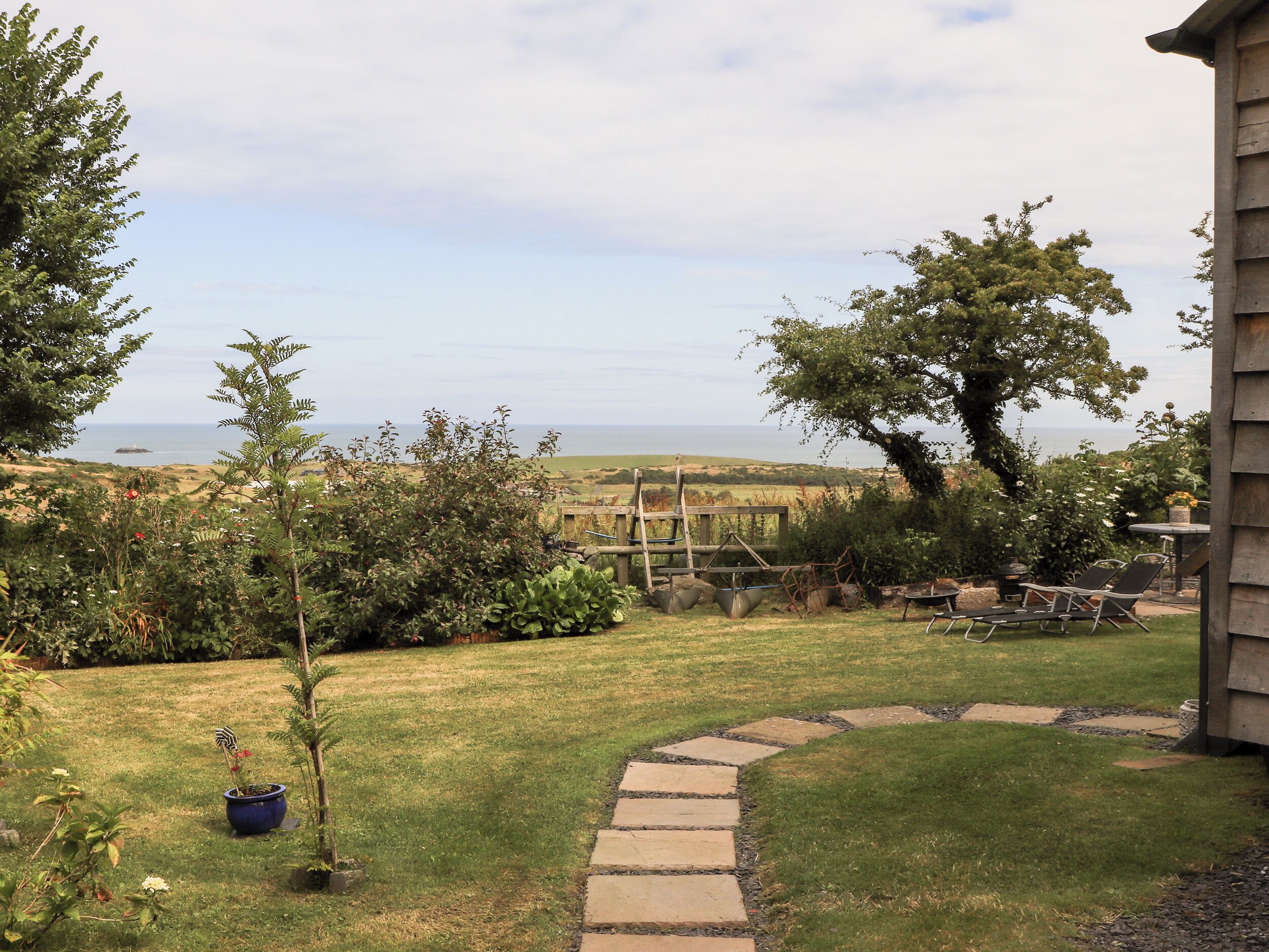 A garden with a stone pathway leading to a wooden deck, overlooking a coastal landscape.
