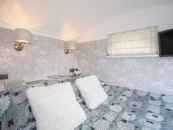 A bedroom with a bed, two wall-mounted lamps, a television, and a window with a curtain. - Shepherds Stone (Holyhead)
