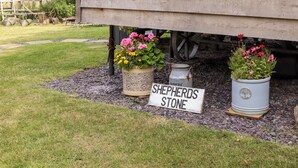 A rustic wooden structure with a sign reading "SHEPHERDS STONE" and two flower pots with pink flowers. - Shepherds Stone (Holyhead)