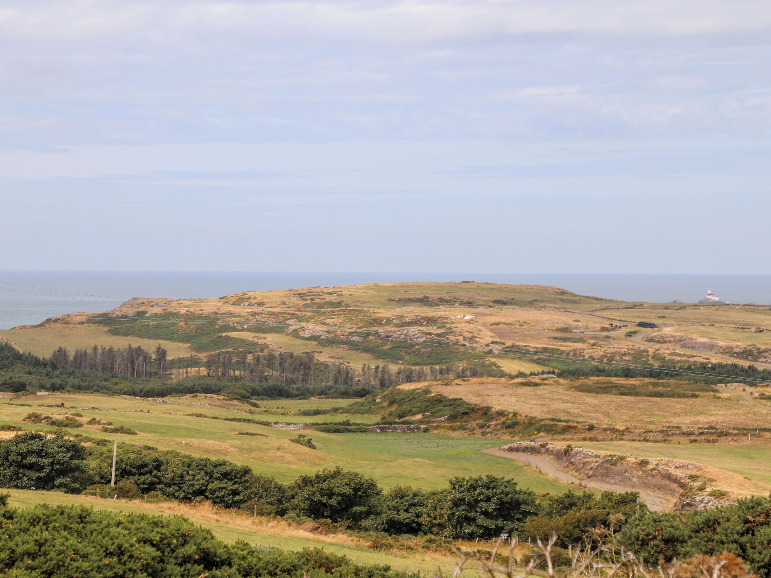 Paisaje costero con un faro, colinas onduladas y una vista despejada del mar.
