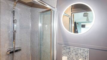 Une salle de bain moderne avec une douche à parois de verre, un miroir rond et un mur recouvert de carreaux.