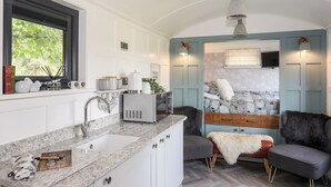 A modern kitchen with a marble countertop, white cabinets, and a window with greenery outside. - Shepherds Stone (Holyhead)