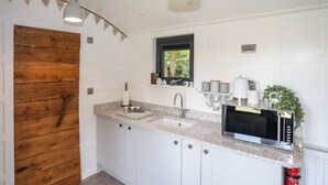A kitchen with white cabinets, a granite countertop, a microwave, and a window with a view of trees. - Shepherds Stone (Holyhead)