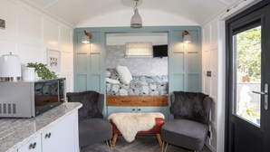 A compact, well-lit room with a bed, two armchairs, a small table, and a kitchenette. - Shepherds Stone (Holyhead)
