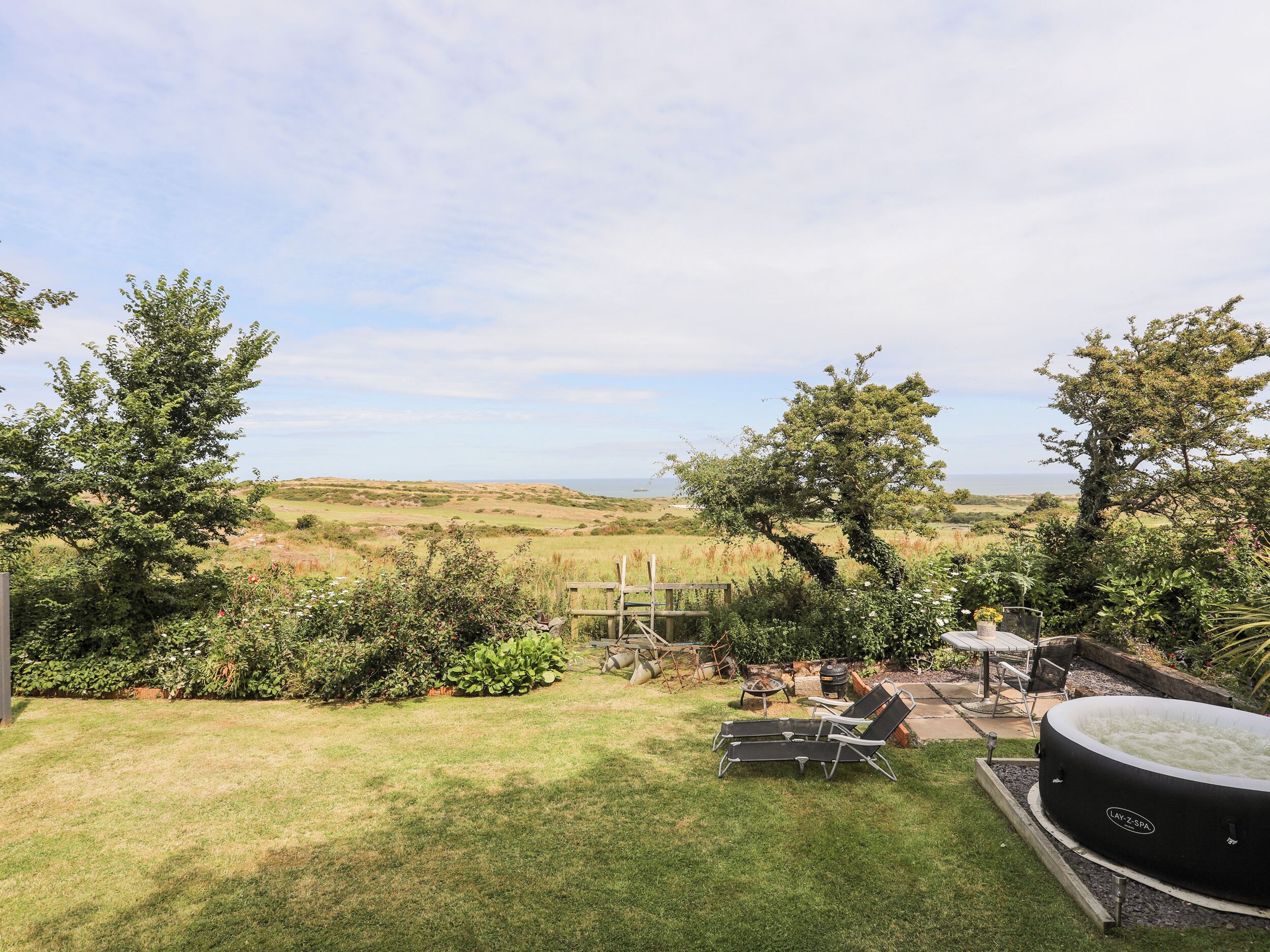 Een achtertuin met een jacuzzi, lounge stoelen en uitzicht op het platteland.