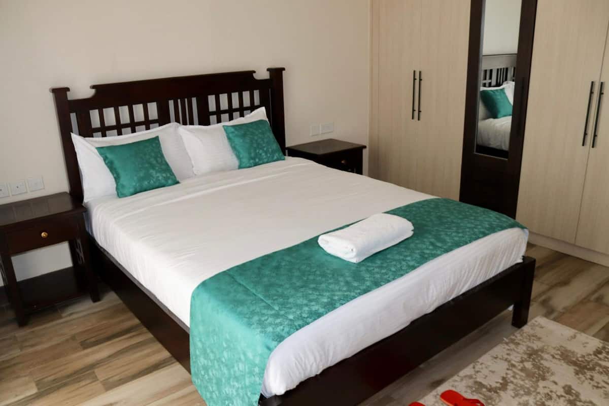 A neatly made bed with white and green bedding, a wooden headboard, and a small bedside table.
