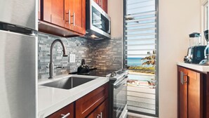 A modern kitchen with a stainless steel refrigerator, a microwave, and a built-in oven. There is a large window with a view of a pool and palm trees.