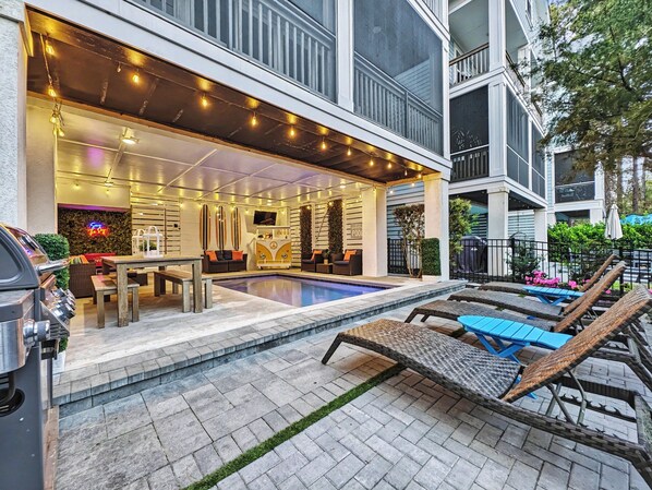 A poolside area with lounge chairs, a barbecue grill, and a pool.