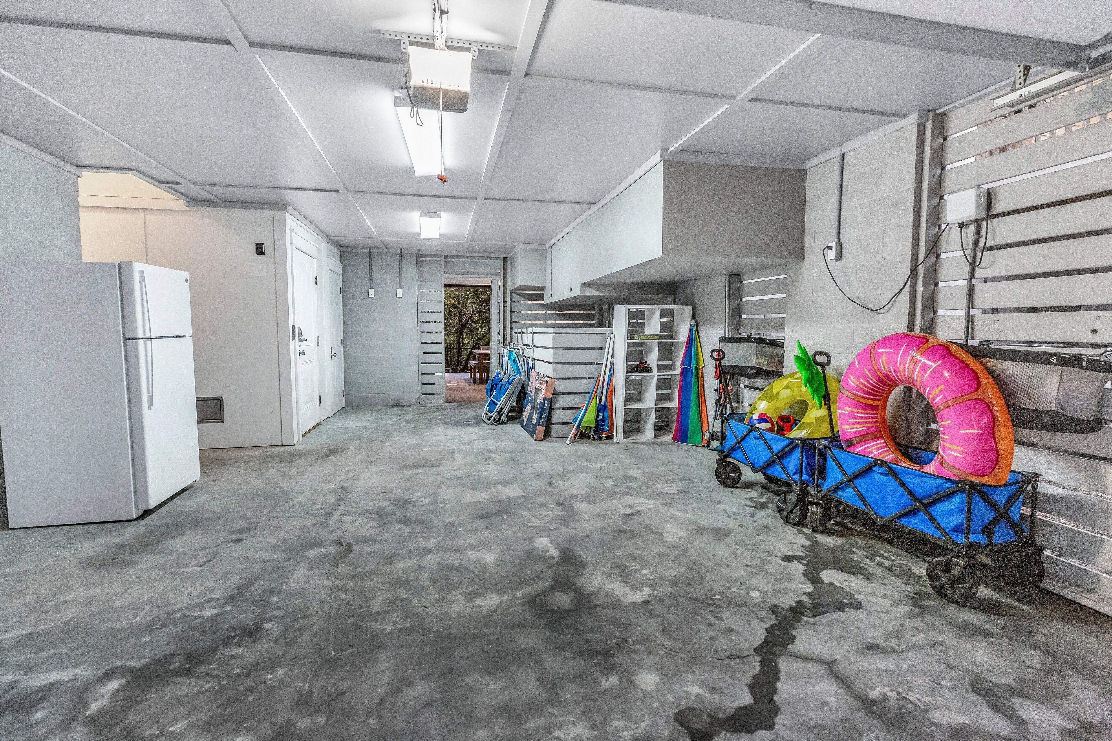 A spacious garage with concrete floors, a white refrigerator, and a blue cart with inflatable rings.