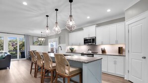 A modern kitchen with white cabinets, a central island, and pendant lighting. - 13SC Beach, Private Pool, 10 foot movie theater screen (Hilton Head Island)