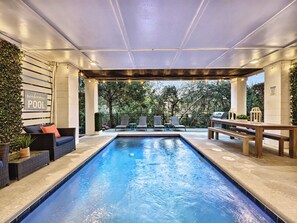 Zona de piscina con un letrero que dice 'Welcome to our POOL', rodeada de sillas de descanso y una parrilla.