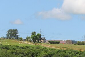 Een landelijk landschap met een boerderij, een stenen schuur en een tractor op het land.
