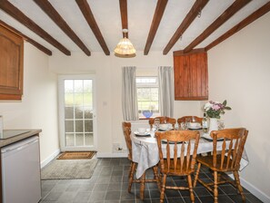 Een eethoek met een tafel voor vier personen, houten stoelen, een houten plafond en een raam met gordijnen.
