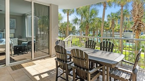 Un balcón con mesa y sillas, con vista a una piscina y palmeras.